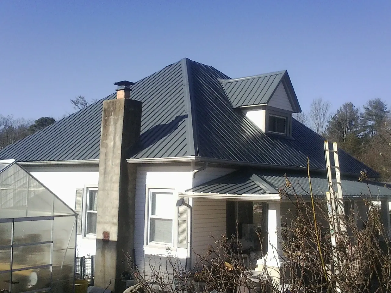 Dark blue standing seam metal roof on a white farmhouse with dormer — Slate & Tile Roof Repair by Roofing Brothers in Erhard