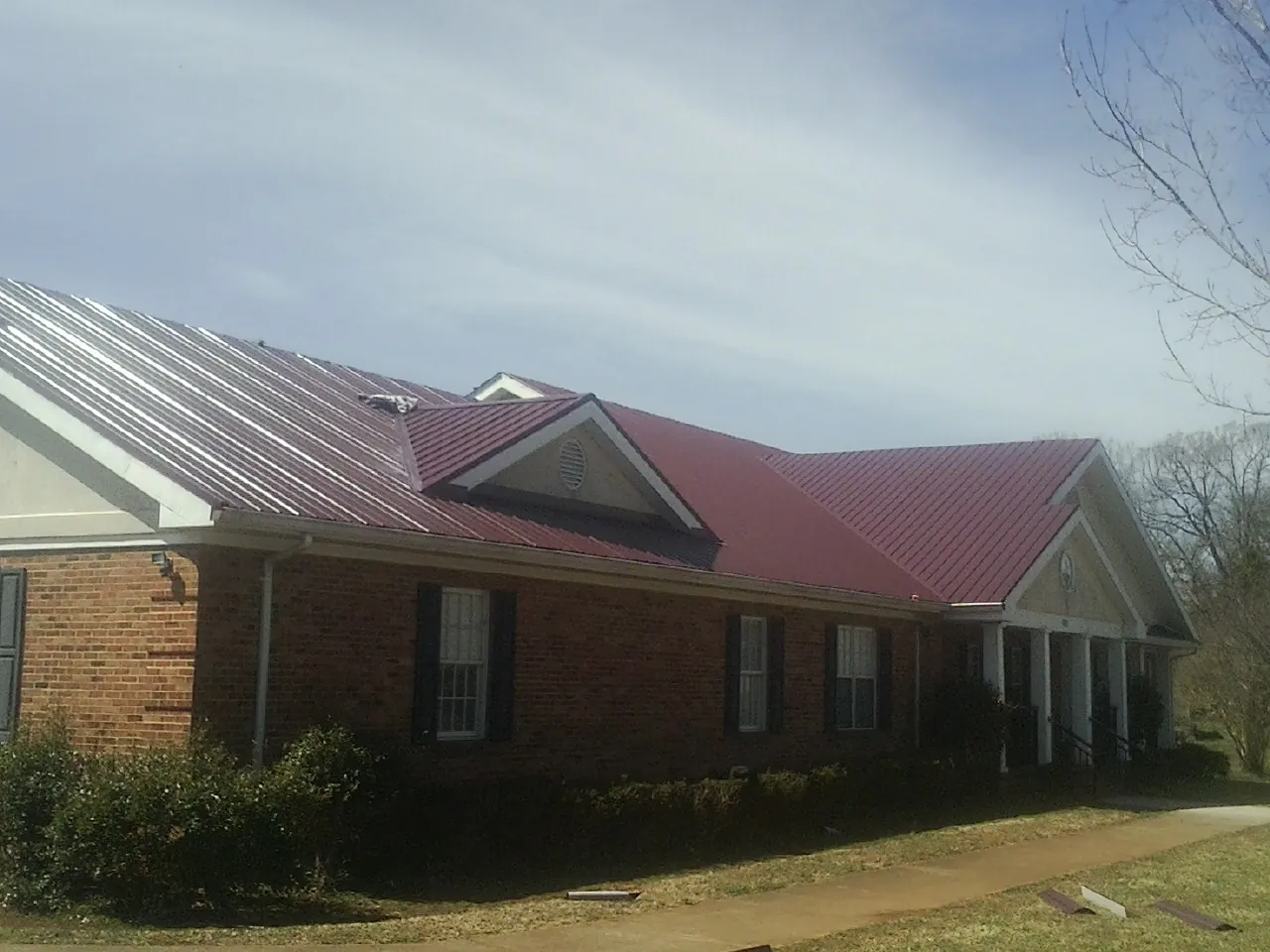 Red metal roof with gabled entries on a long brick building, from a Hail Damage Roof Repair job in Erhard