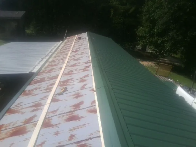 Old rusted panels beside newly installed green metal roofing — Wind Damage Roof Repair by Roofing Brothers in Erhard