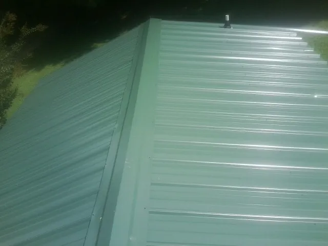 New green metal panels meeting at the ridge of a roof — Flat Roof Repair work by our crew in Erhard