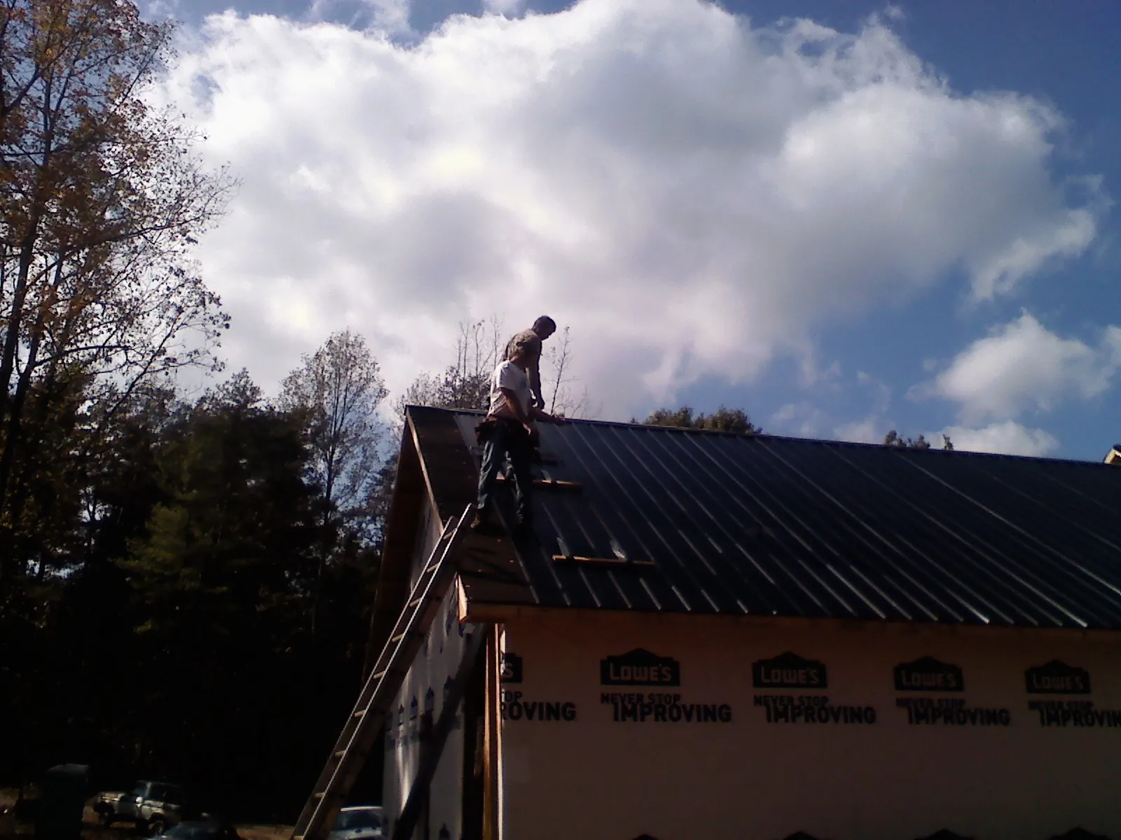 Roofer fastening dark metal panels high against a cloudy sky, from a Roof Inspection job in Erhard