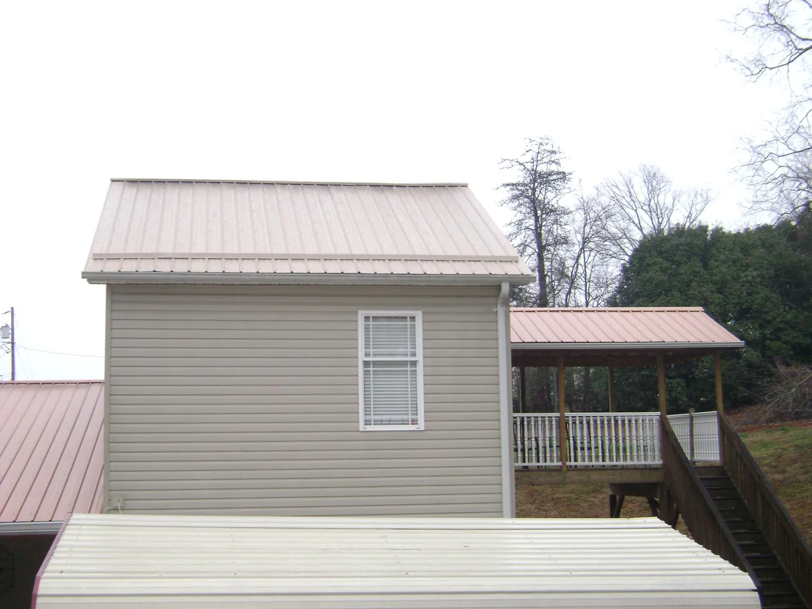 Tan metal roofs on a two story addition and attached porch, from a Roof Replacement job in Erhard