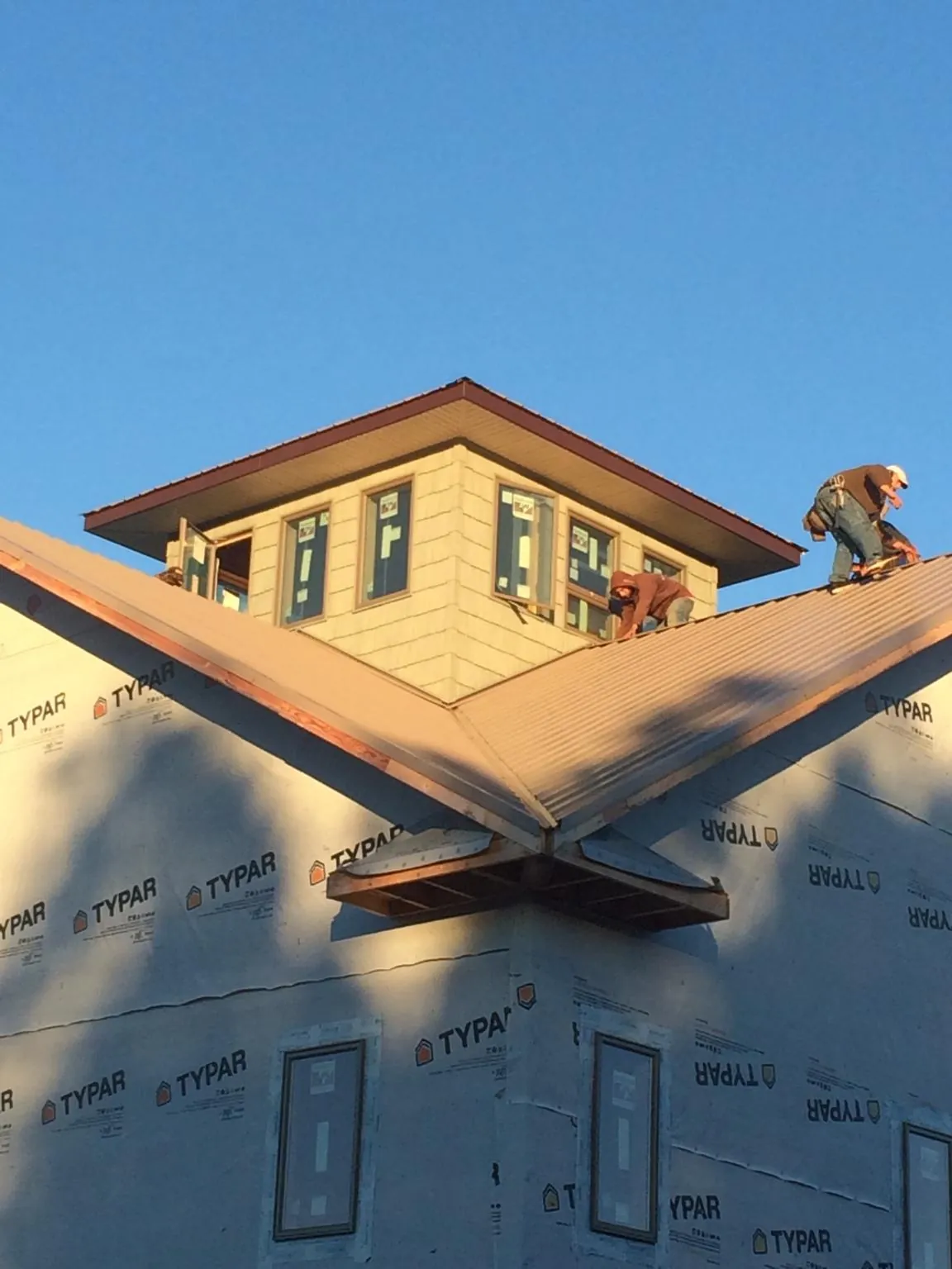 Roofers working around a rooftop cupola on a new metal roof at sunset — Roof Waterproofing in Erhard by Roofing Brothers
